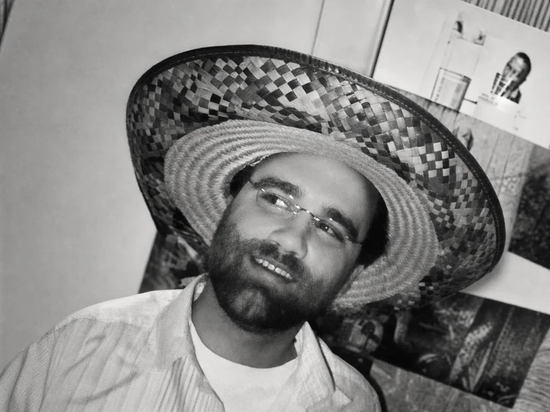 A candid black-and-white portrait of Adam smiling beneath a woven hat.
