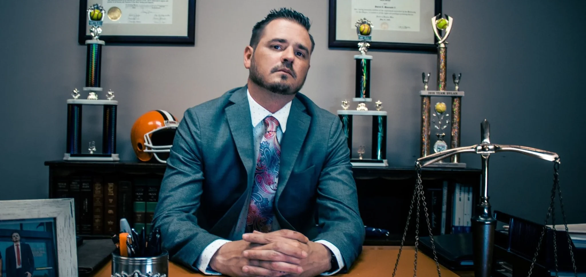 Attorney seated at his desk in an office with framed certificates and legal scales